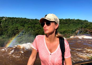 Woman wearing sunglasses looking away standing against waterfall
