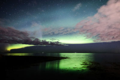 Aurora borealis reflecting on sea against sky at night