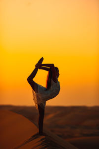 Woman with arms outstretched against sky during sunset