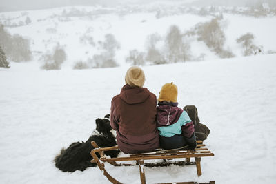Mother and children with border collie sitting on snow covered field against mountain