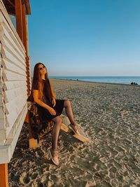 Woman sitting on beach against clear sky