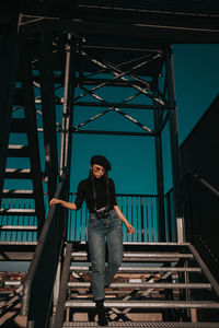 Portrait of young woman standing on steps against sky