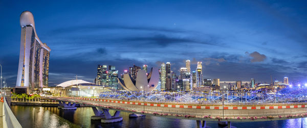 Illuminated bridge over river by buildings against sky at night