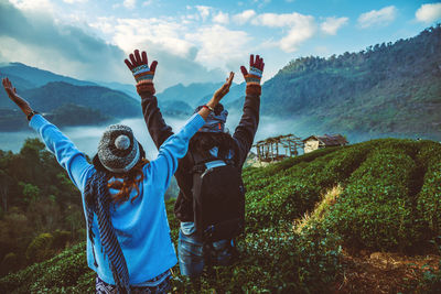 Rear view of couple with arms raised standing against sky