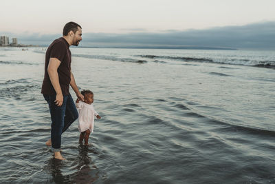 Full length of father and son at beach against sky