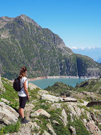 Hiker standing on rock by lake and mountains against sky