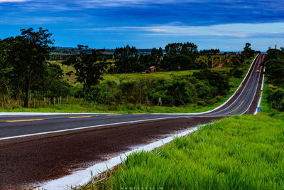 Road by trees on landscape against sky