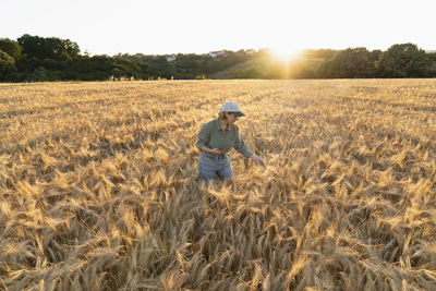 Woman holding digital tablet in field at sunset examining barley ear