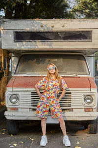 Confident female in trendy summer overall standing near old abandoned caravan and looking at camera