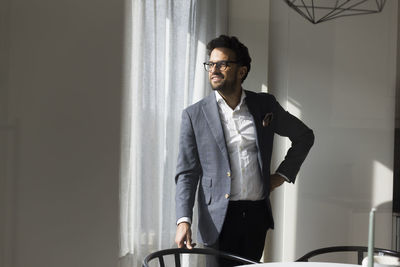 Smiling male real estate agent standing with hand on hip in new home