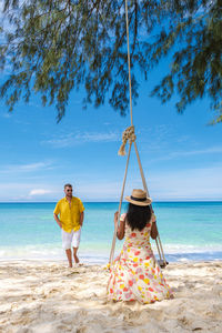 Rear view of woman swinging at beach against sky