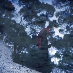 Reflection of woman holding umbrella in puddle during rainy season