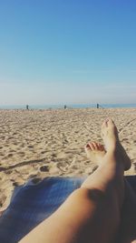 Low section of woman relaxing on beach against clear sky