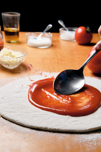 Pouring tomatoes on a homemade pizza base to prepare in the oven