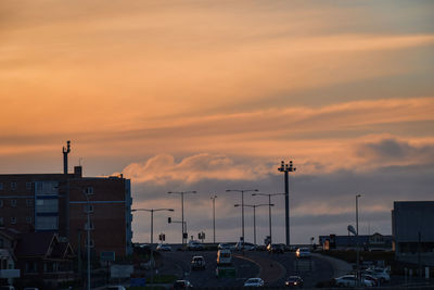Cars on road by buildings against orange sky