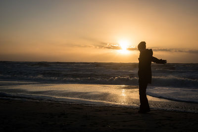 Man standing on shore at beach against sky during sunset