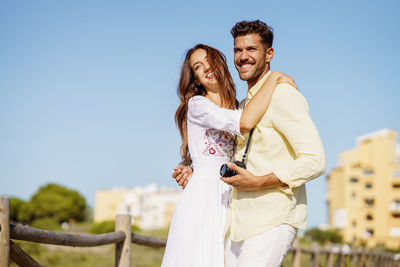 Smiling couple standing against clear blue sky during sunny day