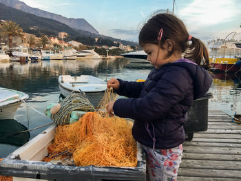 Side view of girl playing with fishing net at jetty by lake