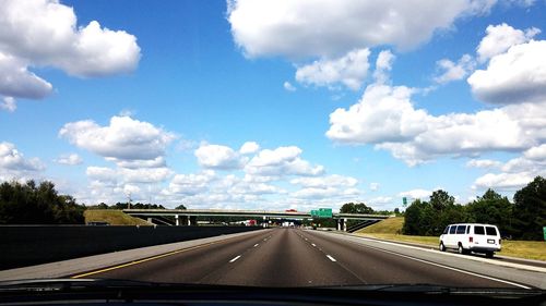 Road passing through highway against cloudy sky