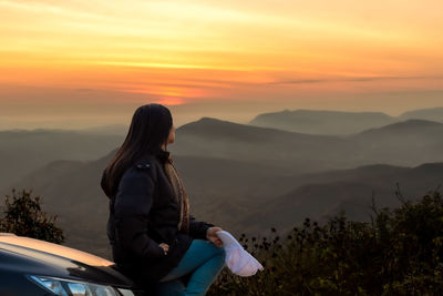 Woman standing on mountain against sky during sunset