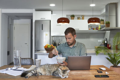 Businessman eating noodles while cat sleeping at dining table