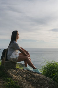 Side view of young woman looking at sea against sky