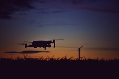 Silhouette drone flying over plants against sky during sunset