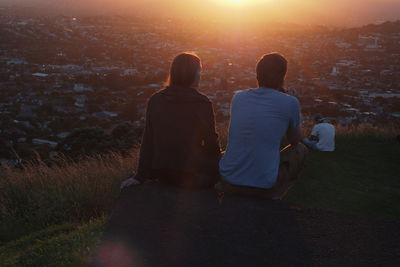 Rear view of man sitting on field against sky during sunset