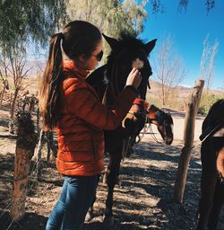 Side view of young woman pampering horse on field