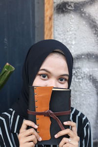 Portrait of young woman holding camera while standing outdoors