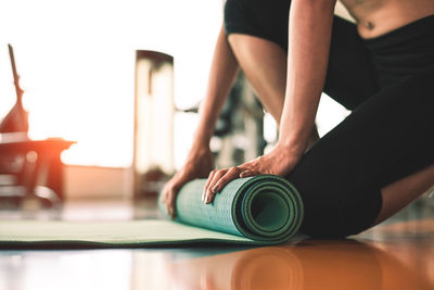 Midsection of woman folding exercise mat on floor in gym