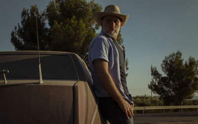 Portrait of adult man in cowboy hat standing against a vintage car