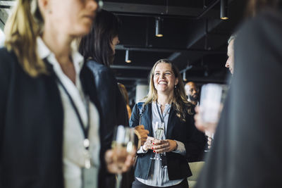 Smiling female business person talking with coworkers while holding drink at workplace