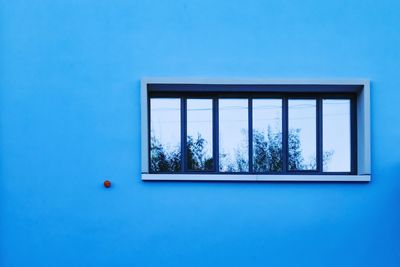 Blue wall with a window reflecting the sky. 