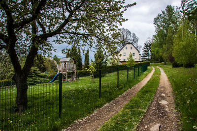 Footpath amidst trees on field against sky