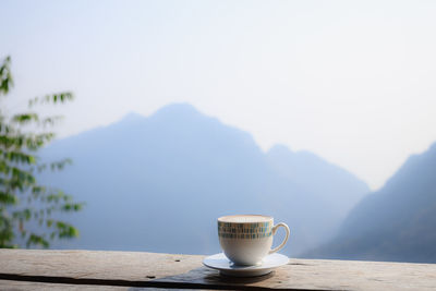 Hot coffee cappuccino in white cup on wooden terrace with beautiful scenic view nature background 