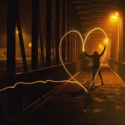 Woman doing light painting on heart shape at illuminated bridge