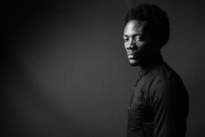 Portrait of young man looking away against black background