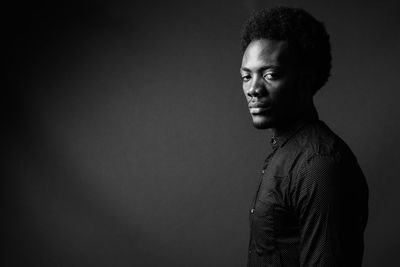 Portrait of young man looking away against black background