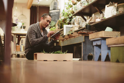 Worker using tablet computer while sitting on floor in plant shop