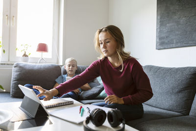 Teenager using digital tablet while brother using phone at home