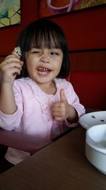 Portrait of smiling girl gesturing thumbs up while making a face at home