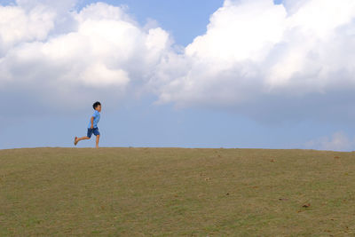 Side view of boy walking on grass against sky