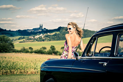 Rear view portrait of mid adult woman wearing sunglasses while standing by car against hill