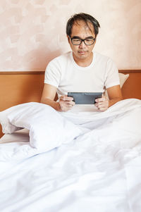 Mature man using digital tablet while sitting on bed at home