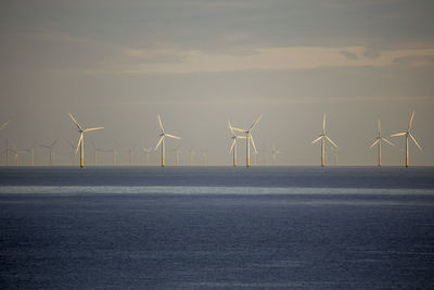 Wind turbines by sea against sky during sunset