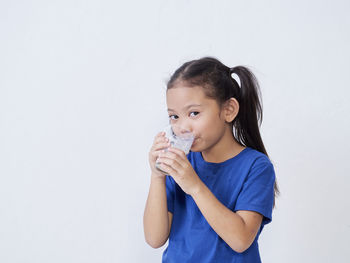 Portrait of cute girl drinking water against white background