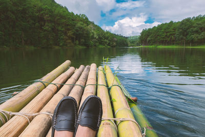 Low section of person on wooden raft in lake against sky