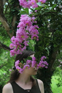 Young woman looking away while standing against flowering plant