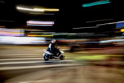Blurred motion of person riding motorcycle on illuminated city at night